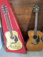 Academy 41" guitar shipping box standing next to Raven acoustic guitar leaning against a wooden dresser