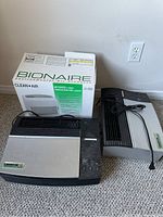 Photo of one Bonaire air purifier with box and two Oreck XL air purifiers on carpeted floor.