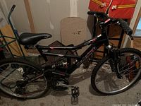 Side view of the black Raleigh mountain bike showing frame, saddle, rear wheel, pedals, and tires.