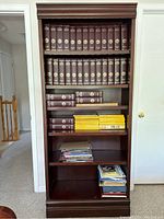 Front view of the wooden bookshelf filled with encyclopedias, magazine files, and miscellaneous papers.