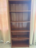 Front view of wooden bookcase showing all five shelves and some visible wear on the surfaces.