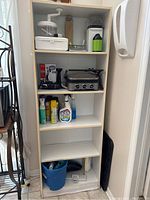 Front view of white bookshelf filled with various household items to illustrate shelving and condition, showing water damage at base