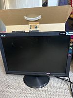 Black 19 inch ASUS computer monitor on a round base stand, front view, with cardboard box behind.