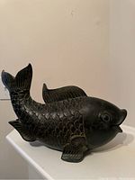 Side view of the black decorative fish sculpture highlighting its textured scales and open mouth.