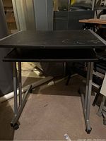 Front view of one black rolling desk showing tabletop and metal legs with wheels.