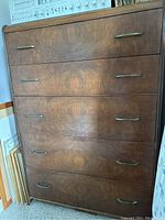 Front view of the wooden dresser showing five drawers with metal handles and visible wear.