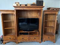 Front view of the wooden TV cabinet and the two side bookcases with a 55-inch TV placed inside for scale.