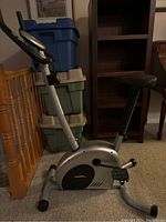 Side view of silver stationary exercise bike showing frame, pedals, seat and flywheel housing