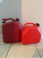 Photo of two red plastic gasoline containers side by side, one larger and one smaller, both with black screw caps and handles.