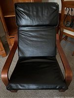 Front view of Ikea Poang chair showing black leather seat and headrest cushion with bentwood armrests and frame.