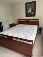 Front angle of queen sleigh bed with mattress in a bedroom, including nightstand and lamp.