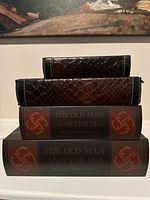Stacked view of three hollow storage books showing front spines and covers, two titled 'The Old Man and The Sea' and one smaller with crocodile-skin texture.