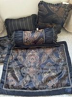 Black set of decorative pillows including several types with patterned fabric and fringe, plus pillow shams