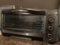 Front and side view of Hamilton Beach toaster oven showing main glass door and three control knobs on the side.