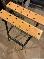 Workbench with wooden top featuring round holes, a protractor and ruler markings on a black metal frame.