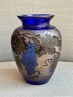 Front side view of the cobalt blue art glass vase showing the grape cluster and leaf motif on the rounded body with flared rim.