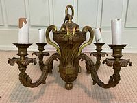 Front view of antique French brass chandelier showing four ornate arms with candle sleeves and central decorative column.