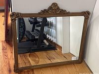 Full view of the large rectangular antique mirror with a gold ornate frame showing detailed scrollwork at top center and curved corners