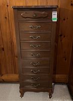 Full view of tall wooden lingerie chest with eight drawers and ornate brass handles, standing on carved legs.