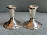 Pair of two antique sterling silver candlesticks standing upright, showing height and overall shape with polished finish and decorative beaded edges.