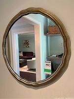 Full view of round wall mirror with wavy gold gilt frame reflecting interior room.