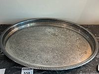 Oval silver tray with decorative floral engravings and monogram M.O.N.Y. on surface, pierced gallery rim visible.