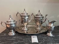 Full view of the entire silver tea set on a black marble surface, showing teapot, coffee pot, sugar bowl, creamer, and tray.