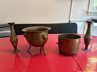 Wide shot showing all four items together on a red table: two tall vases, one three-legged planter, and one bucket.