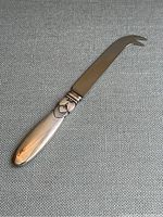 Full view of the cheese knife showing the curved blade and cactus patterned handle on a textured fabric background.