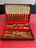 Full view of the open wooden box with gold plated flatware arranged inside, showing knives, forks, spoons, and serving pieces.