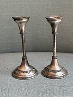 Front view of two vintage sterling silver candlesticks with decorative detailing at base and rim, showing shape and condition including slight bend on one candlestick.