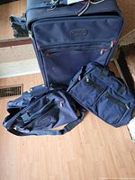 Photo of the full set of three navy luggage pieces, showing a large wheeled suitcase behind two smaller carry-on bags on a wooden floor.