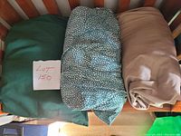 Three queen size sheet sets folded and placed side by side on a wooden surface; solid green, blue-green leaf pattern, and solid beige.