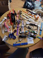 Photo showing a large variety of wristwatches, including analog and digital with multiple colors and band styles laid out on a table.