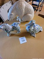 Photo of all three ceramic figurines on a table: white textured bear, blue floral painted horse, and blue floral painted duck.