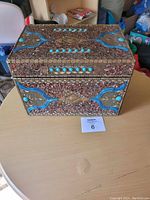 Photo of the box closed showing its detailed jeweled design with turquoise colored stones and metallic ornamental accents on the exterior.