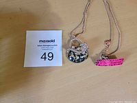 Photo showing Betsy Johnson purse pendant on chain with auction lot number card.
