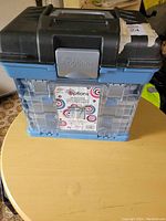 Closed view of the craft/parts case showing the black top lid with a handle and the blue base with a label.