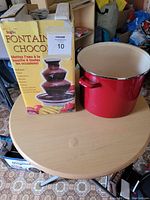 Photo showing boxed Tingly chocolate fountain and large red enamel pot on round table