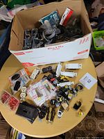 Box containing various electrical components including outlets, switches, wall plates, and wiring connectors scattered on a round table.