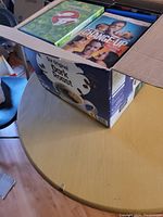 Box containing over 30 DVDs in their original plastic cases, showing 2 visible movie titles on top.