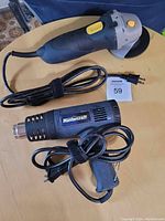 Mastercraft grinder and heat tool laid out on a round wood table. Both cords are coiled neatly with velcro straps. Marwood lot tag #59 visible.