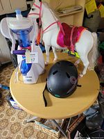 Photo of Black & Decker Artic Twister toy, Barbie horse figurine, and black bike helmet on round table.