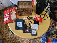 Photo of lot displayed on round wooden table showing all included items: watches, wooden box, ballet slippers, jewelry, mug rack, face mask, and festival-related items.
