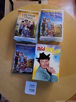 Four DVD cases on a wooden round table: three Little House on the Prairie titles and one Red Skelton Collection.