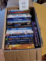 Photo showing the top view of the box containing a stack of DVD cases with visible titles including 'The Ugly Truth', 'Little Women', 'Finding Nemo', 'Spider-Man', 'Walk the Line', 'Bad Lieutenant' among others.