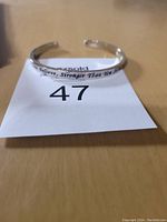 Photo of silver inscribed cuff bracelet on table with lot number 47 visible on paper below