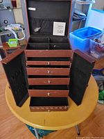 Photo of brown multi-use storage case opened showing top compartment with dividers, four drawers, side doors with slots, and mesh pockets inside lid.