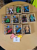 Photo showing 12 Stikbot poseable figurines in original packaging plus two loose figurines on a round table.