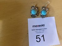 Pair of silver-tone owl earrings with turquoise round stones and rhinestone eyes, displayed on a surface with auction lot number card.